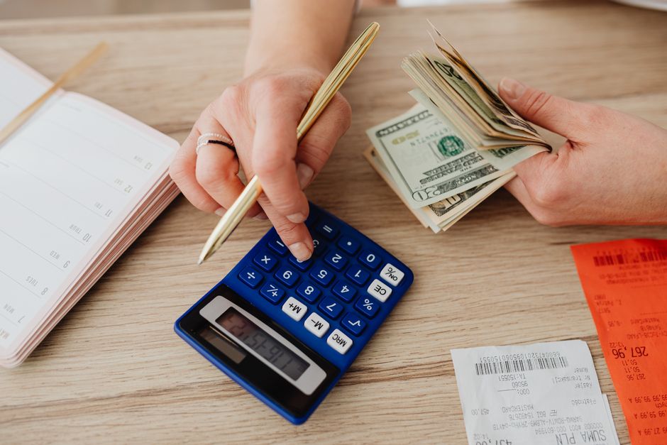 Hands using a calculator with cash and receipts, illustrating an AI video generator pricing comparison and the real cost per finished video