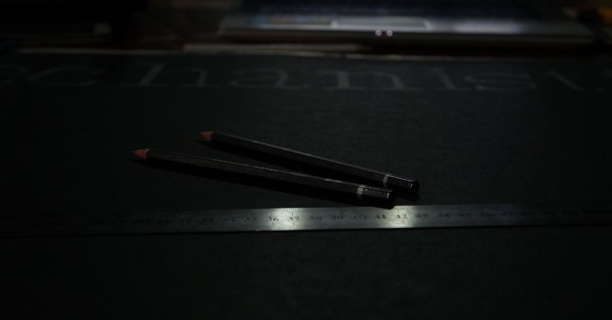 A dark, moody creator workspace with a laptop, pencils and a ruler — designing YouTube thumbnails with AI